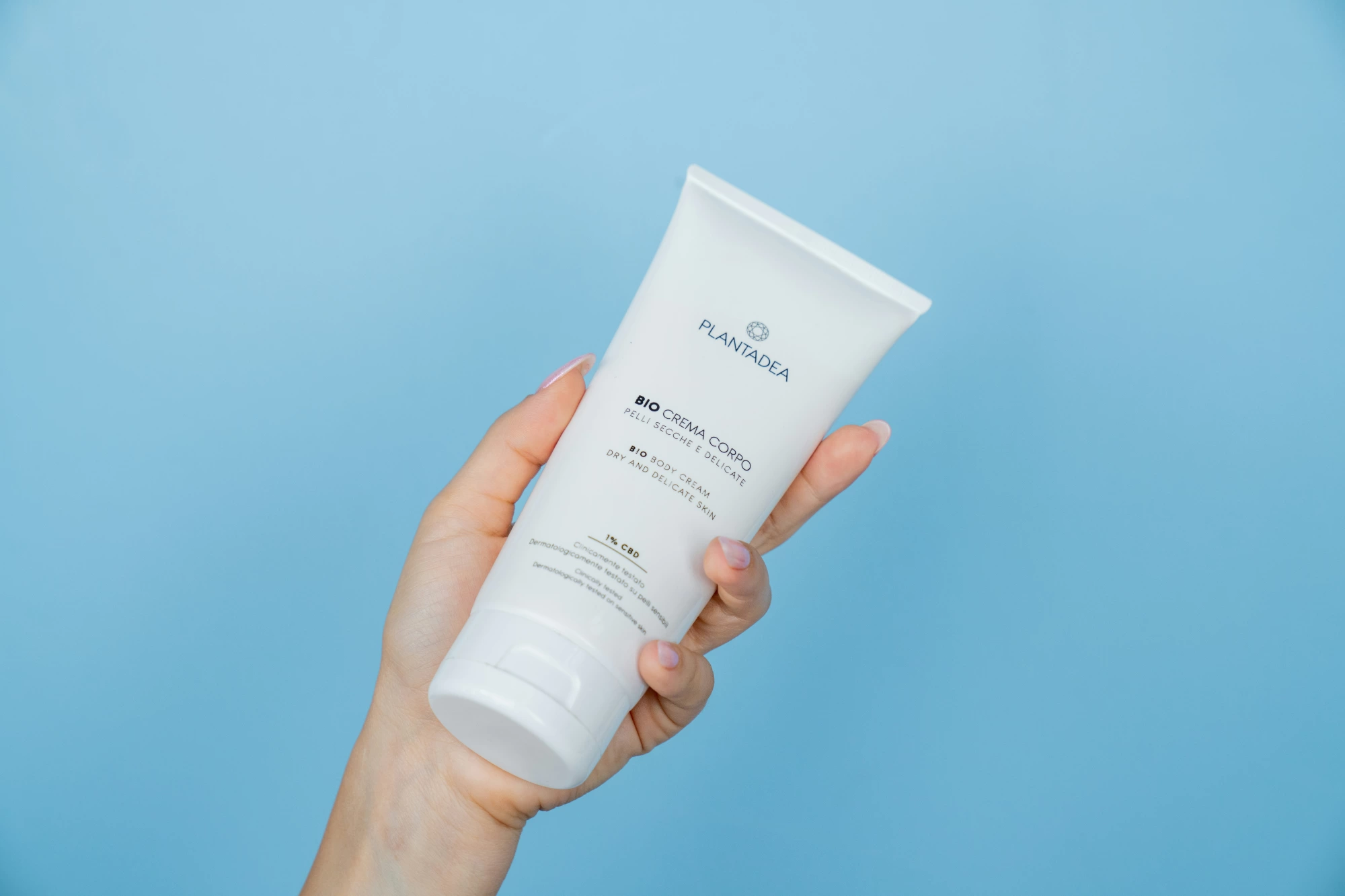Sunscreen tube held against a blue sky, illustrating SPF use in autumn and winter